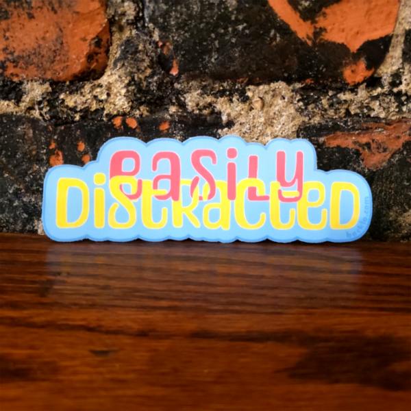 A die cut sticker in blue that says "easily distracted" with easily in magenta and distracted in yellow.