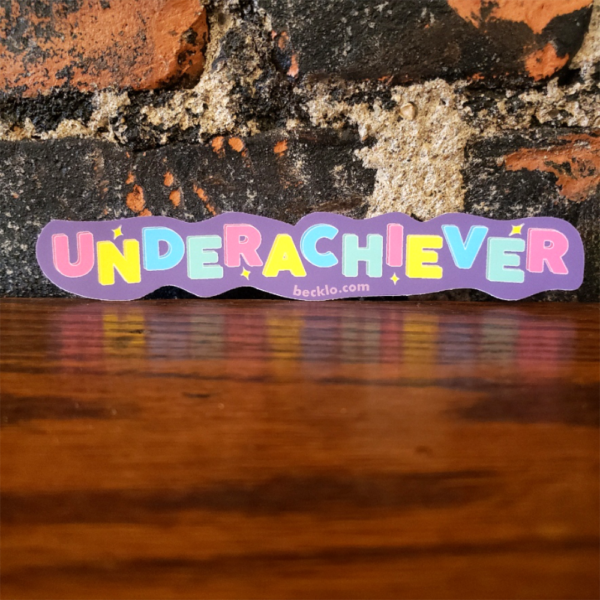 "Underachiever" in pink, yellow, blue, and green alternating letters. Each letter is positioned higher or lower than the next. The background is purple. There are small yellow diamond sparkles in various spots. "becklo.com" is in light purple at the bottom.