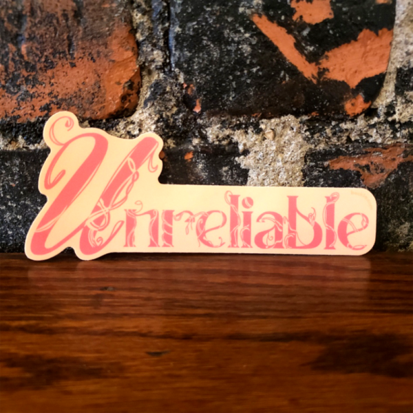 A sticker that says "unreliable" in pink text over a peach background. Vines and wild growth are creeping up each letter, representing stagnation to some, or acceptance of one's limitations to others. There is beauty in making decisions for yourself, even if others don't understand and try to tear you down.